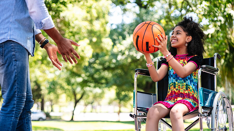 A little girl in a wheelchair having fun with her father while playing basketbal